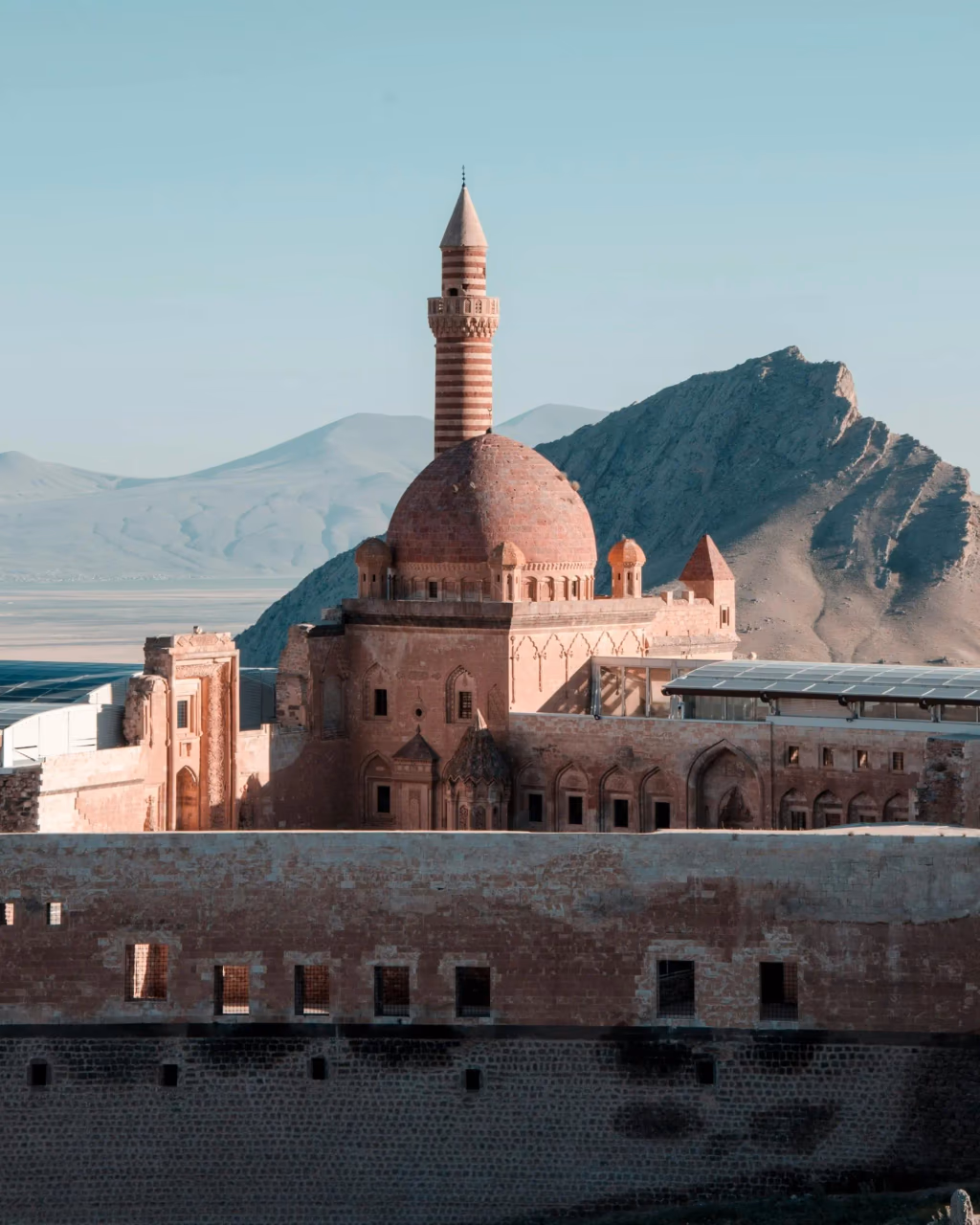 Ishak Pasha Palace with its ornate dome and minaret, set against rugged mountains.