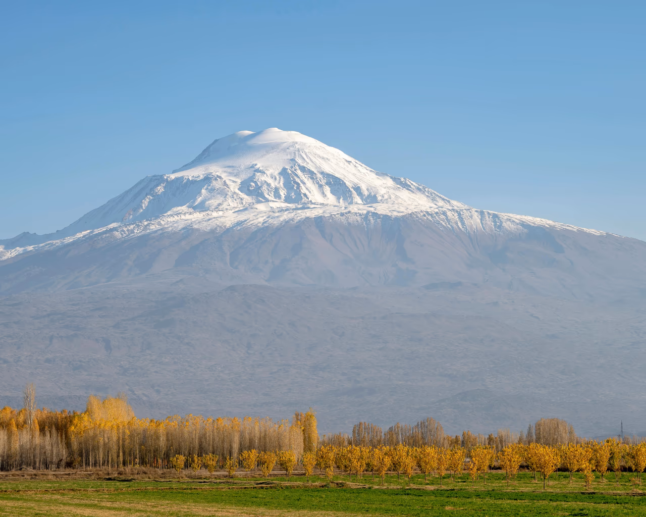 Mount Ararat’s snow-capped peak rising above autumn-colored trees. Blue skies and sun is shining.