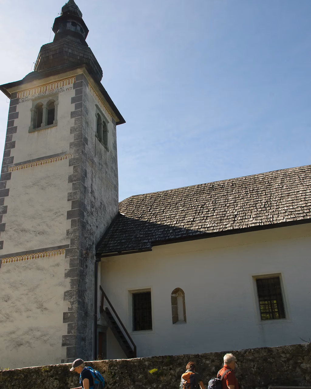 Historic stone church with a tall bell tower, hikers exploring the grounds and reading information signs.