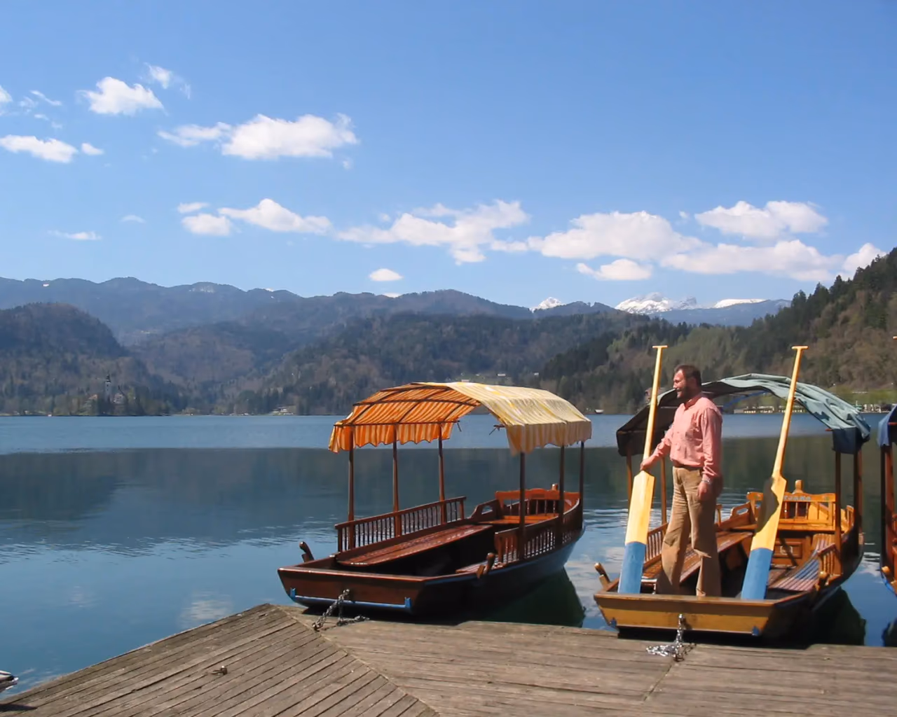 Traditional wooden boats docked at the edge of Lake Bled, with mountain views in the background.