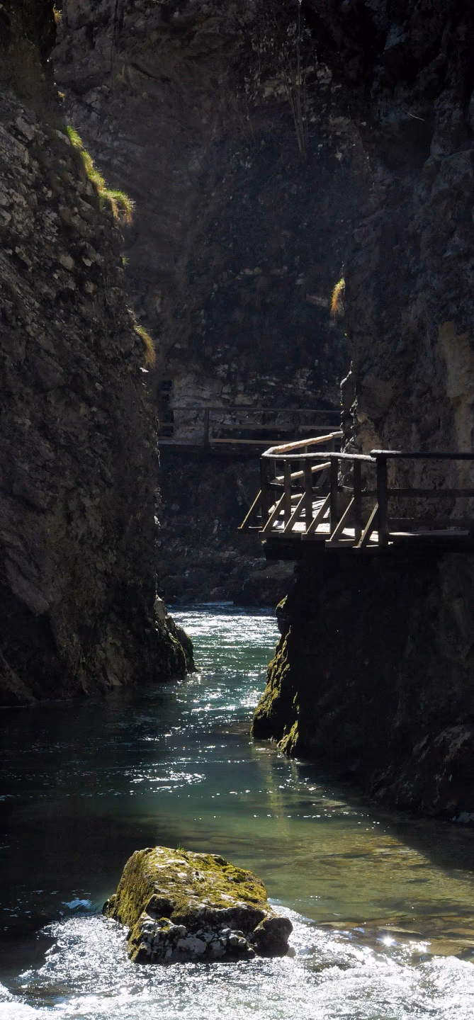 Close-up view of a narrow river canyon with a wooden footbridge hanging over the shimmering water below.