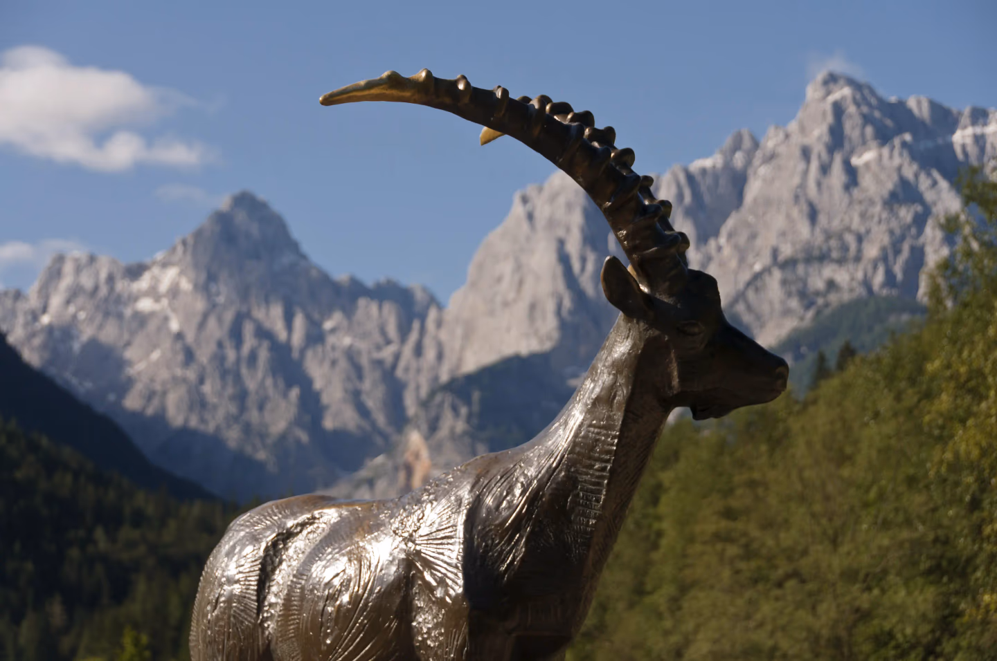 Close-up of ibex statue with Slovenian Alps peaks behind, a scenic stop for hikers and walkers.