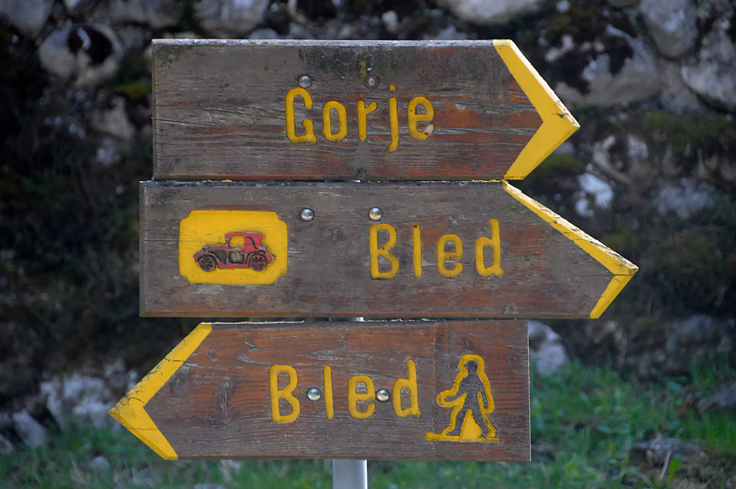 Wooden signpost pointing to Gorje and Bled, with arrows for driving and hiking routes in the Slovenian Alps.