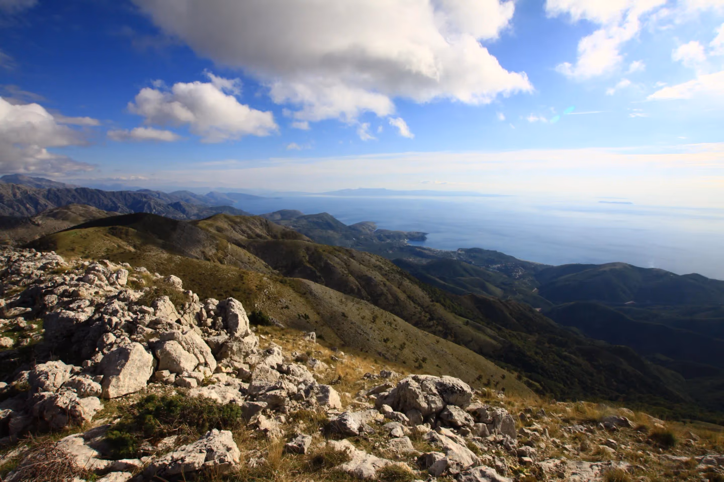 Rocky mountain peaks with rolling green hills and a breathtaking view of the coastline from a hiking trail.