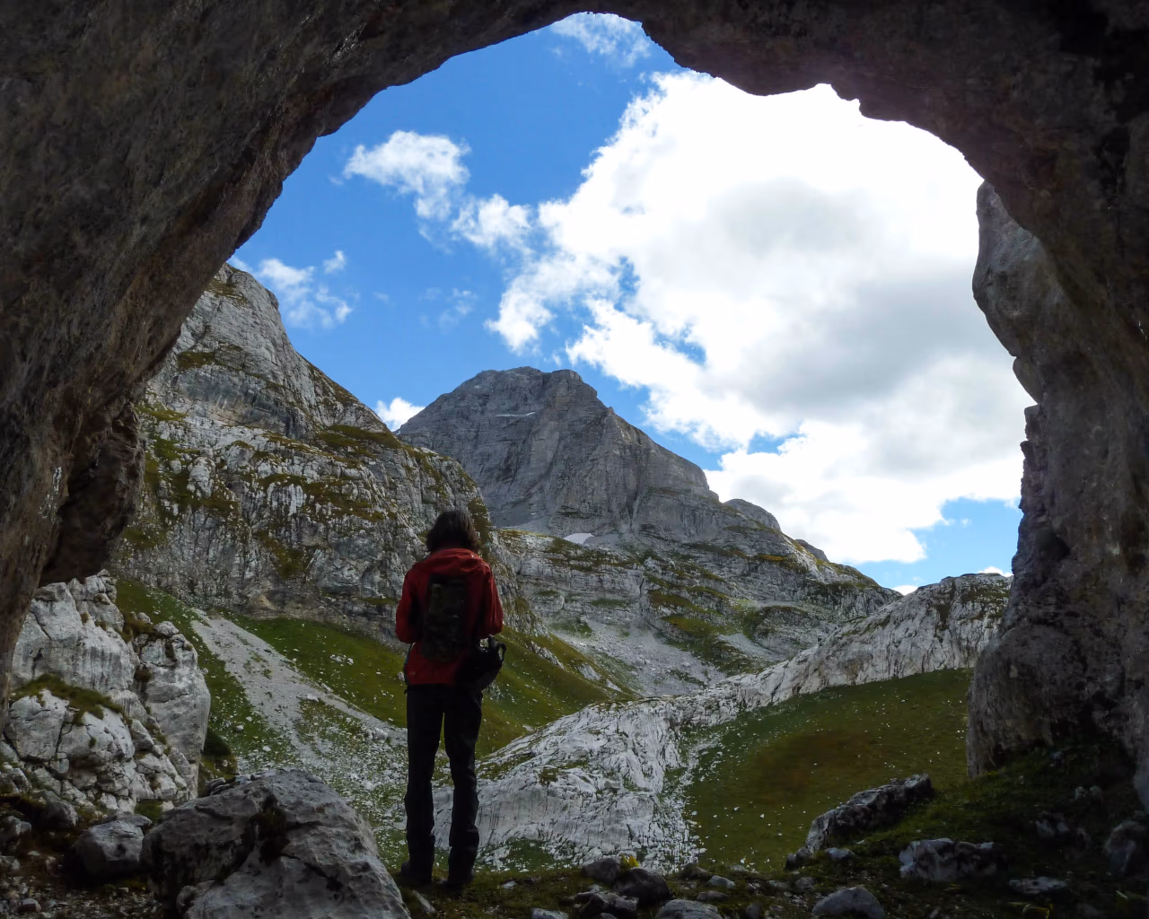 Scenic view of a hiker walking along a high mountain pass in the Albanian Alps, surrounded by towering limestone peaks.