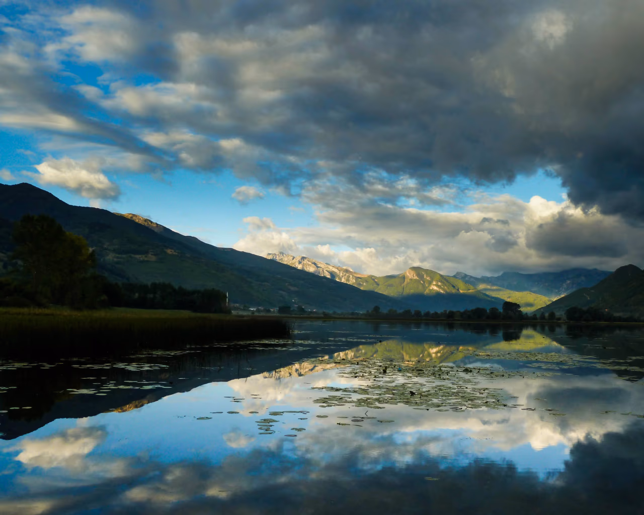 A scenic view of Lake Plav reflecting dramatic clouds and the surrounding mountains in northern Montenegro.