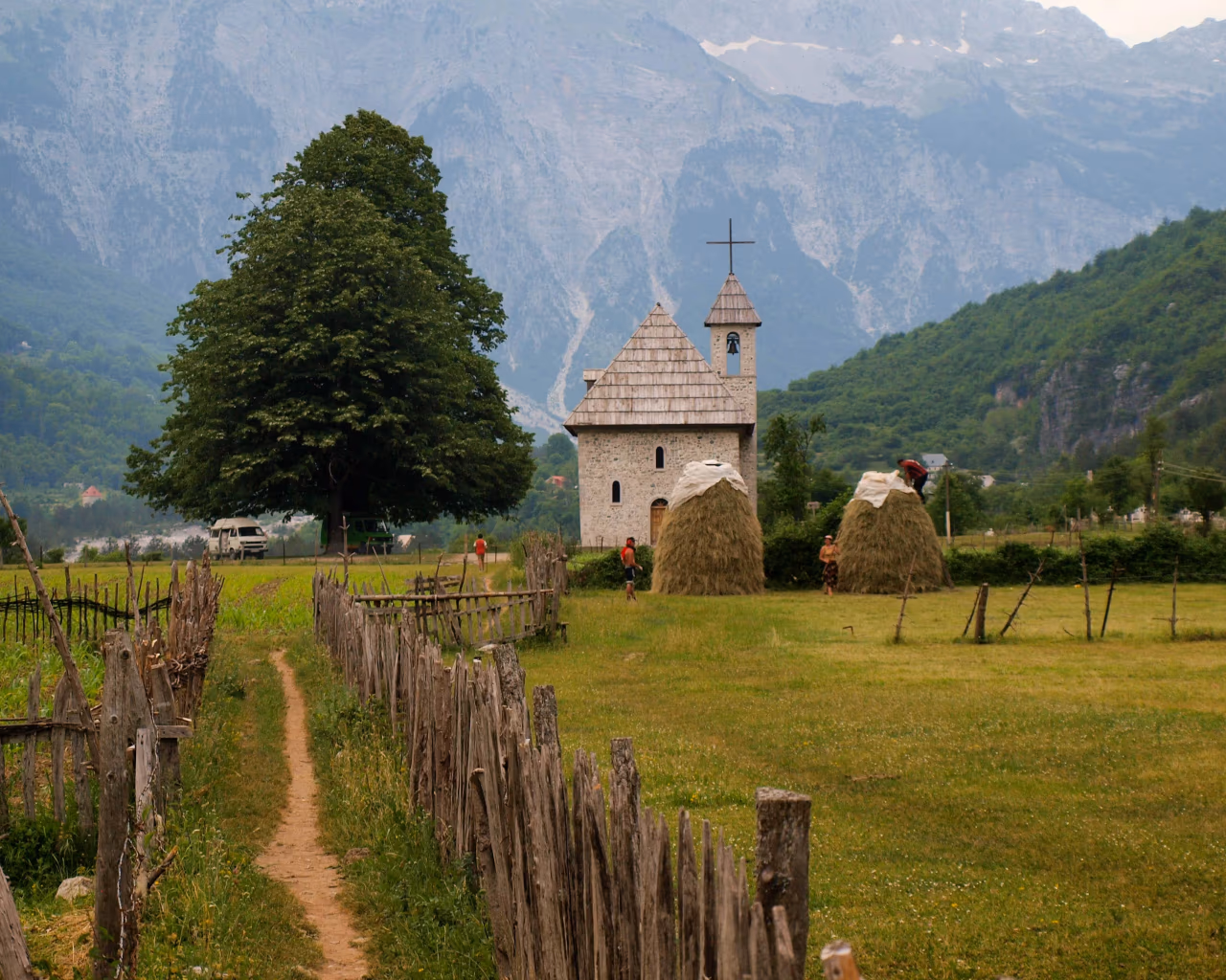 Stone church in Theth village with haystacks and wooden fences amid the Albanian Alps