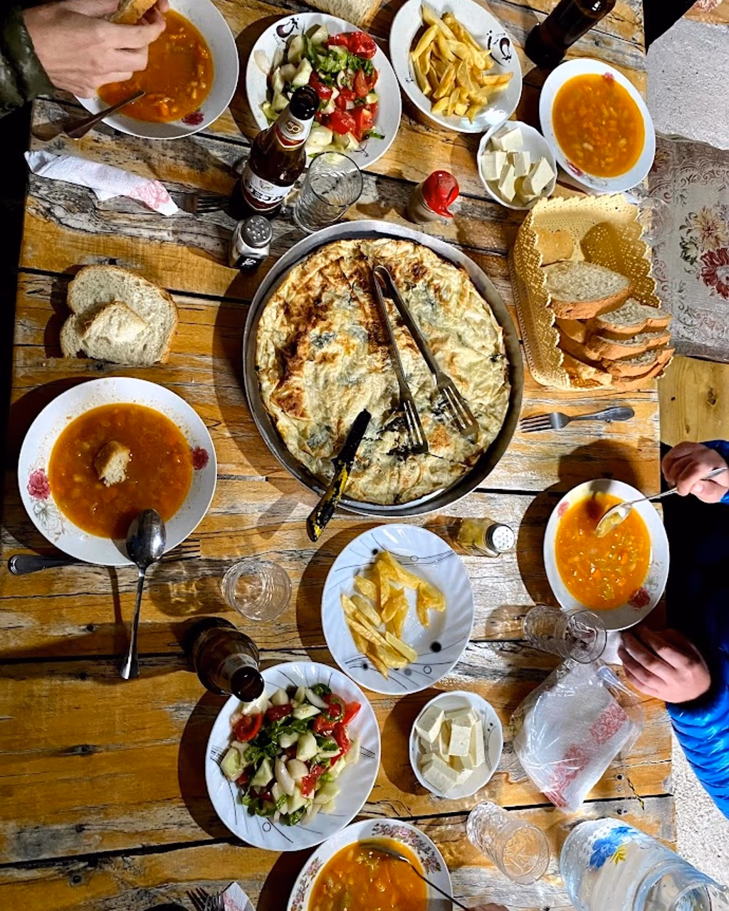 A traditional meal spread with soup, salad, bread, and a large flaky pie on a wooden table.