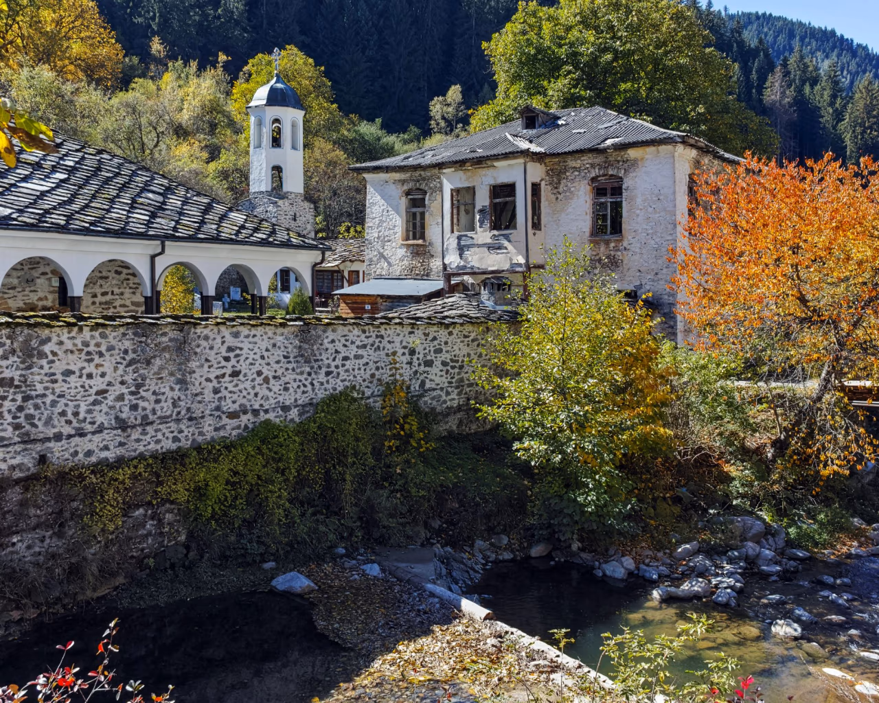 Rhodope Mountains, Bulgaria - A historic stone monastery with a bell tower, surrounded by autumn foliage in the Rhodope Mountains.