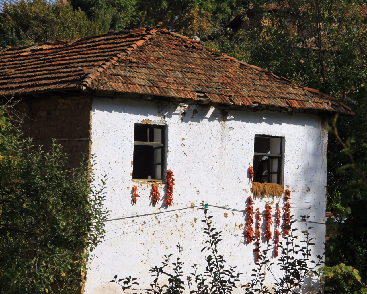An old white-washed house with dried red peppers hanging outside in a remote village.