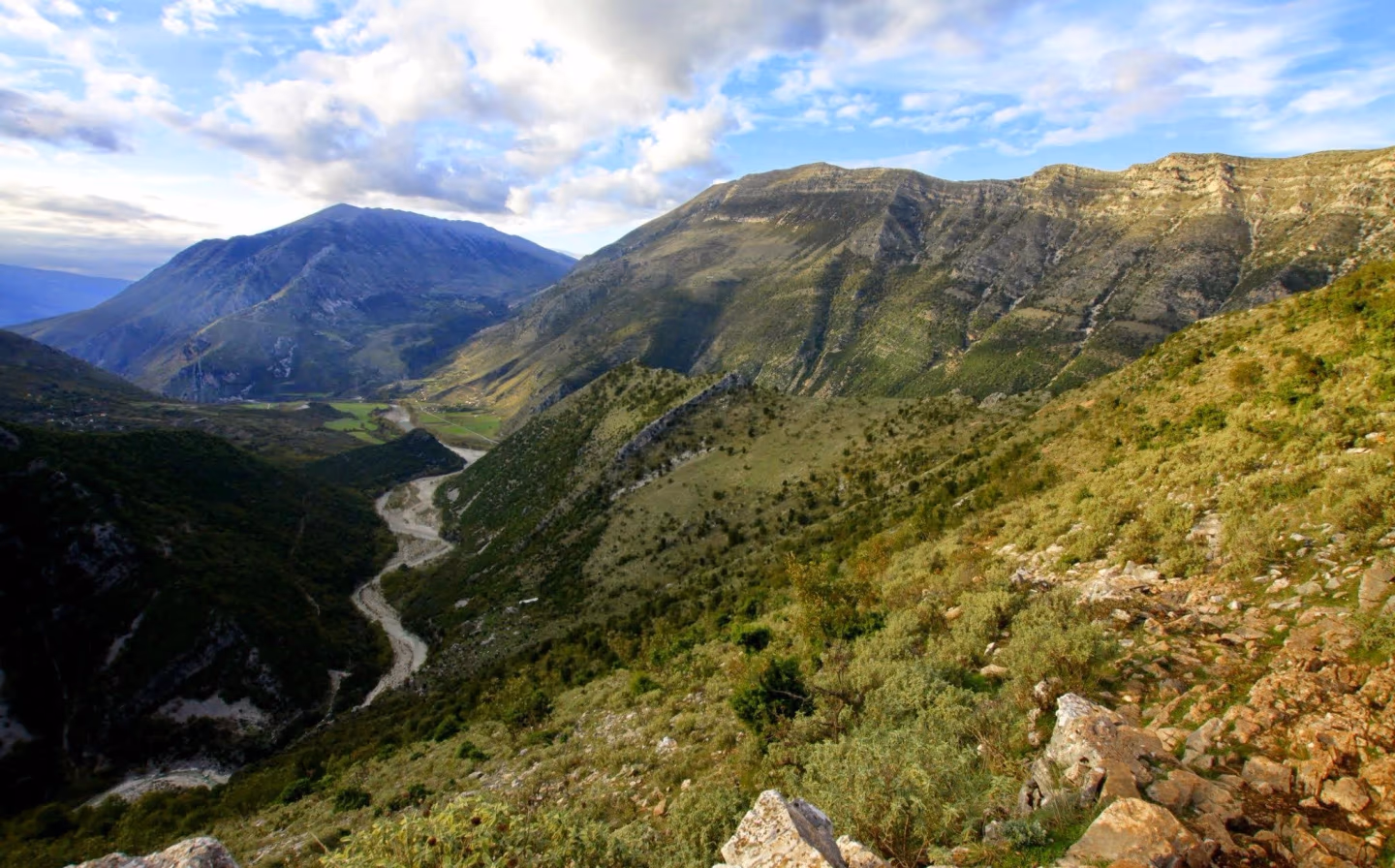A panoramic view of a deep valley with a winding river and distant mountains under a partly cloudy sky.