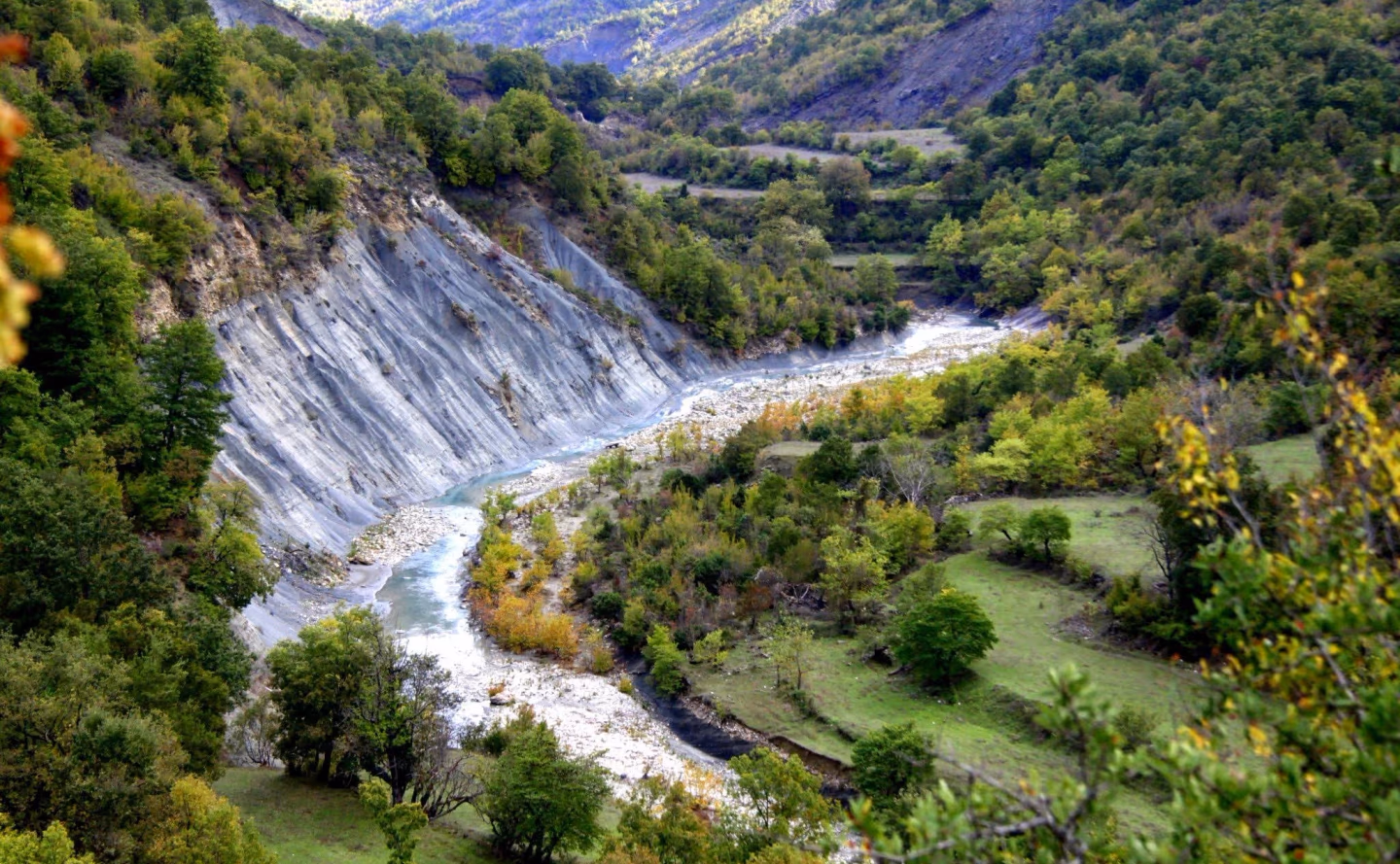 A winding river flows through a lush valley, carving steep rock formations in the Albanian mountains.
