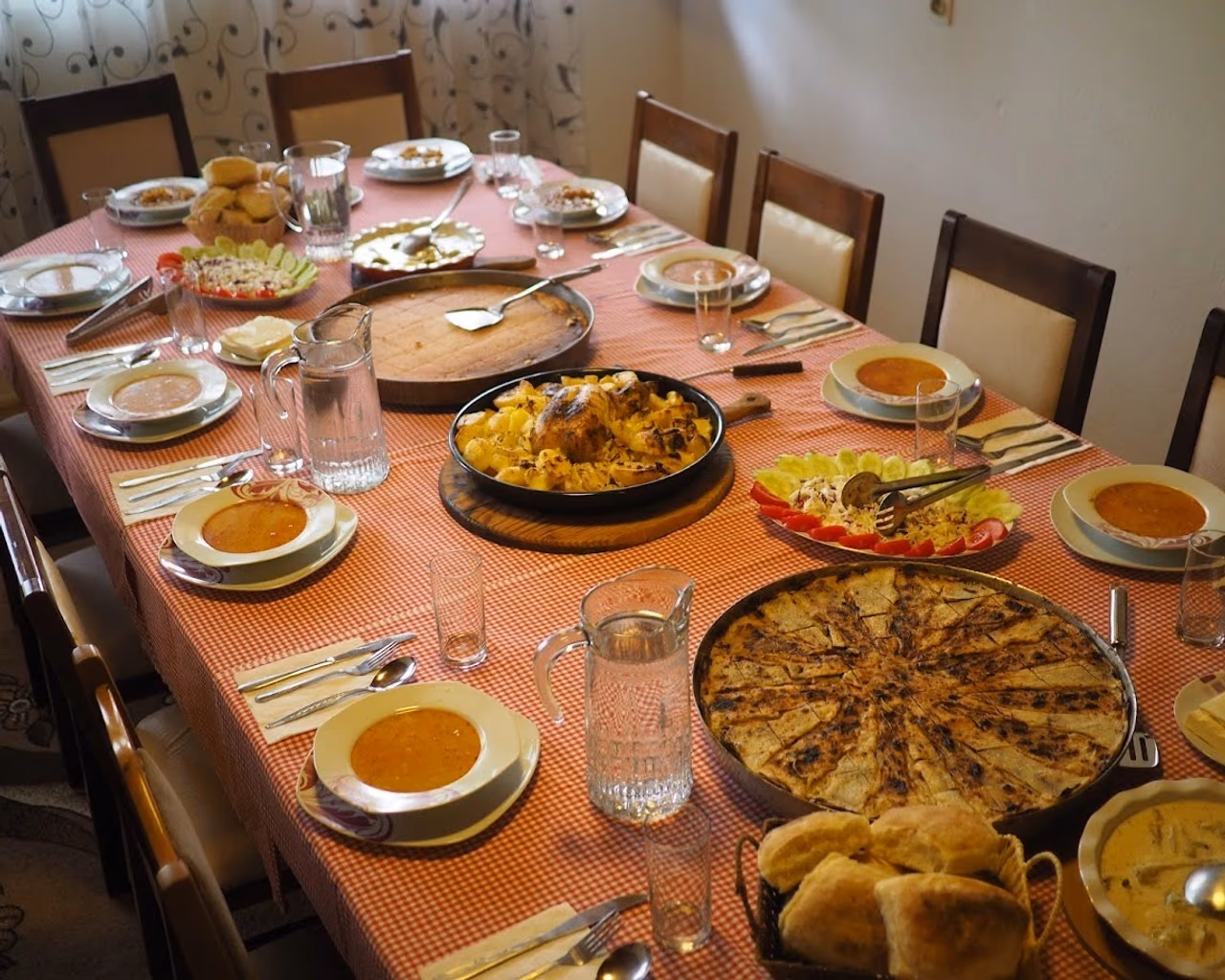 A table filled with homemade dishes, including traditional pies, soups, fresh bread, and salad, set for a meal.