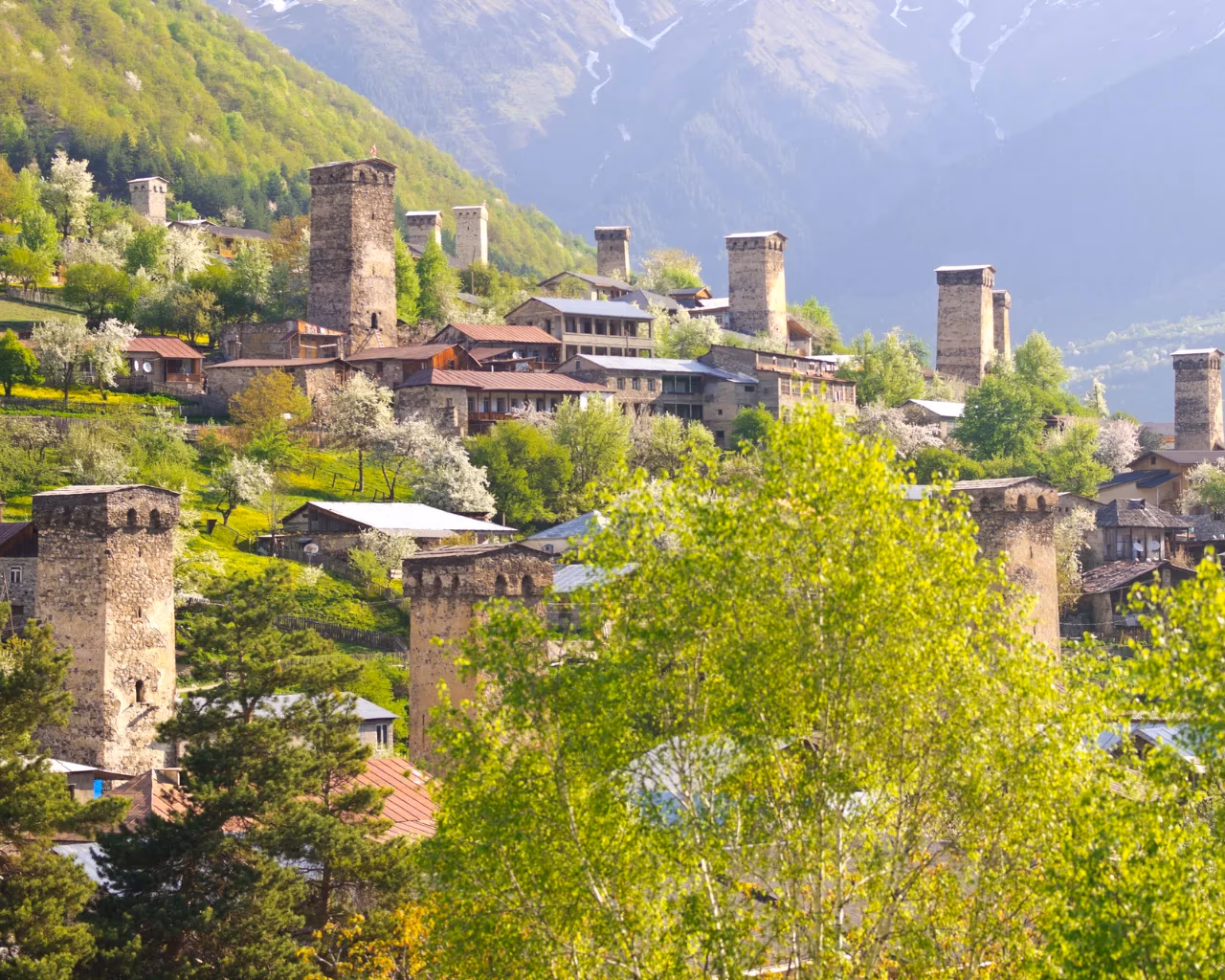 A lush green valley with medieval stone watchtowers in Svaneti, Georgia, set against a backdrop of forested mountains.