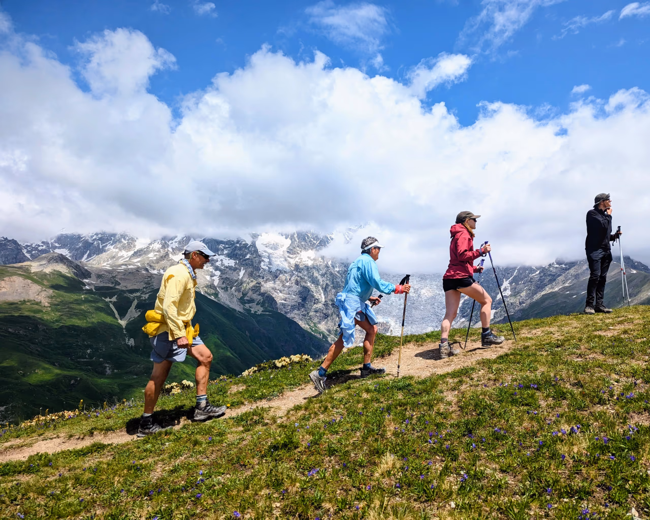 Hikers climbing grassy ridge with trekking poles against backdrop of snow-capped Caucasus mountains