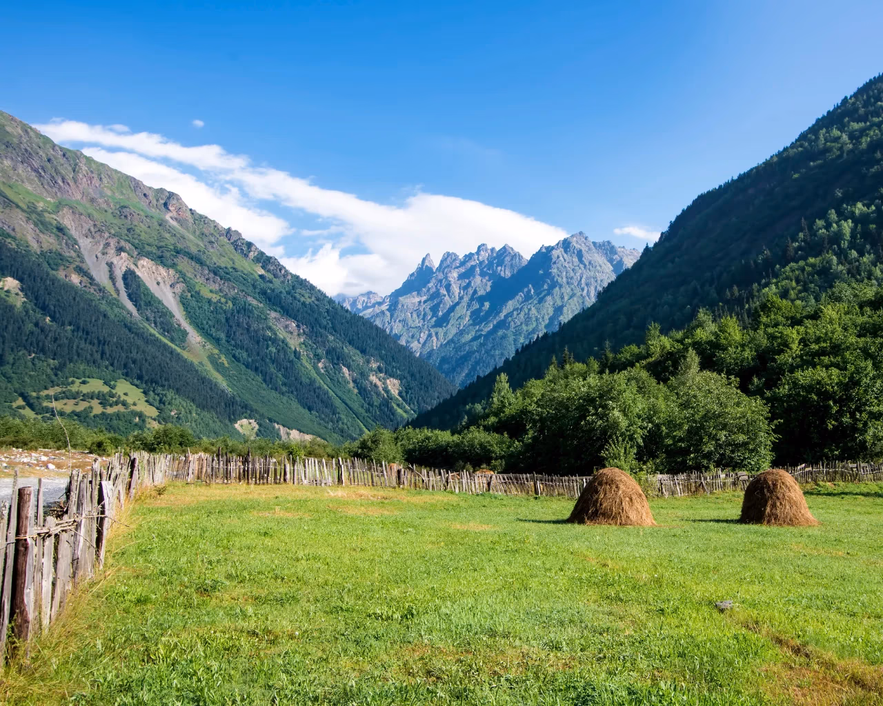 A fenced pasture with haystacks, surrounded by towering green mountains in Svaneti, Georgia.