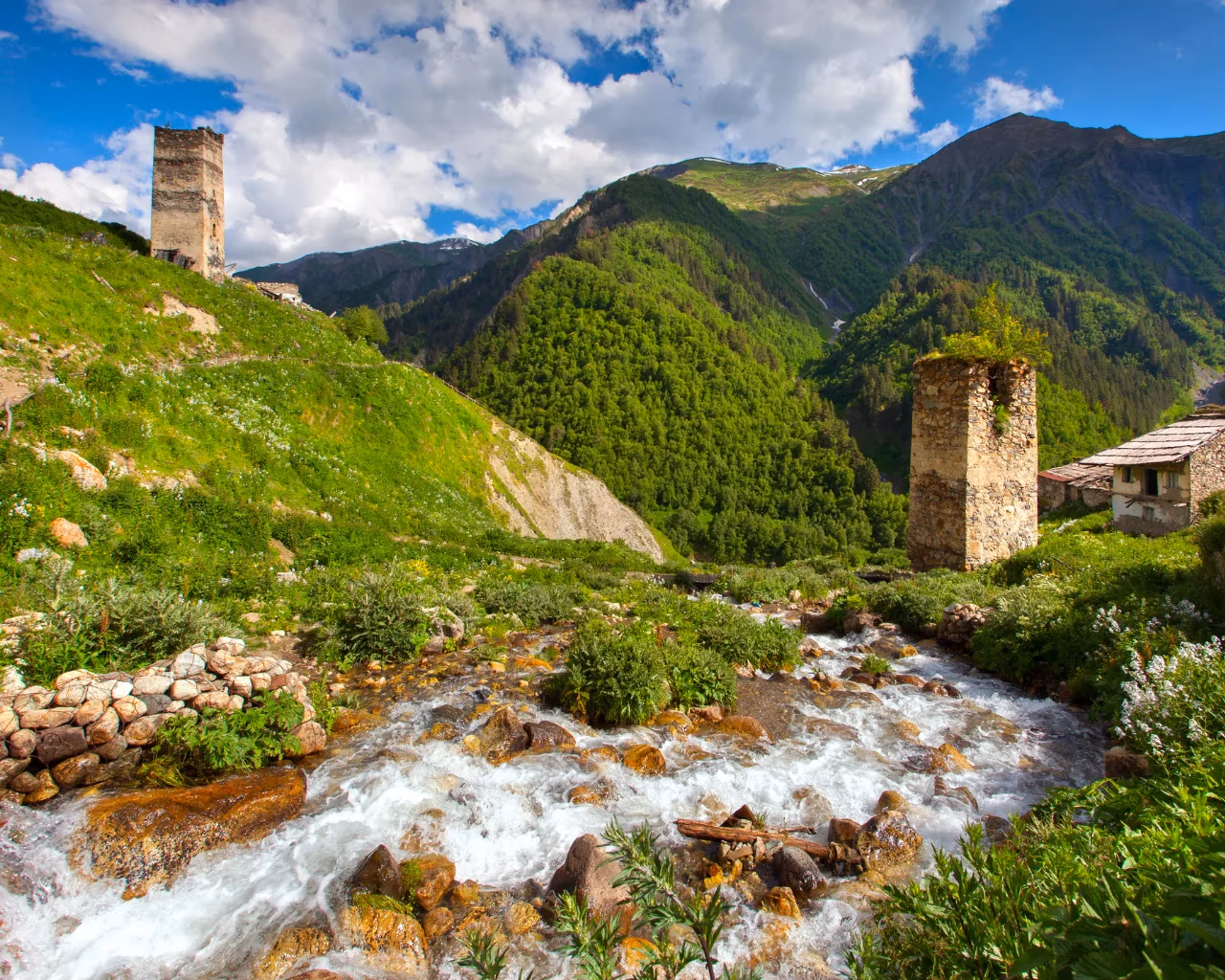 A clear rushing stream flows past ancient Svan towers and lush greenery in a remote valley in Georgia.