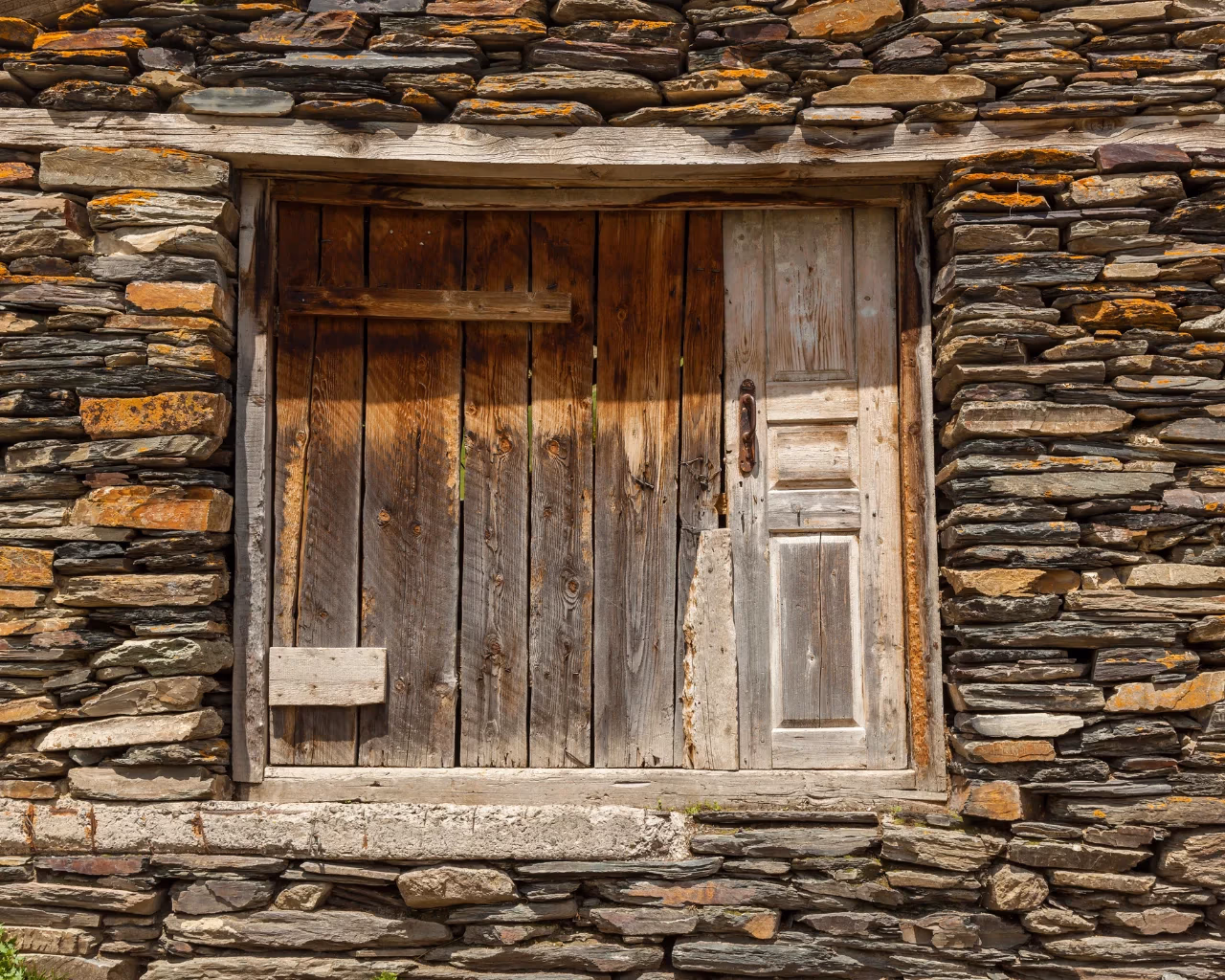 A weathered wooden door set in a stone house in Svaneti, Georgia, showcasing traditional mountain architecture.