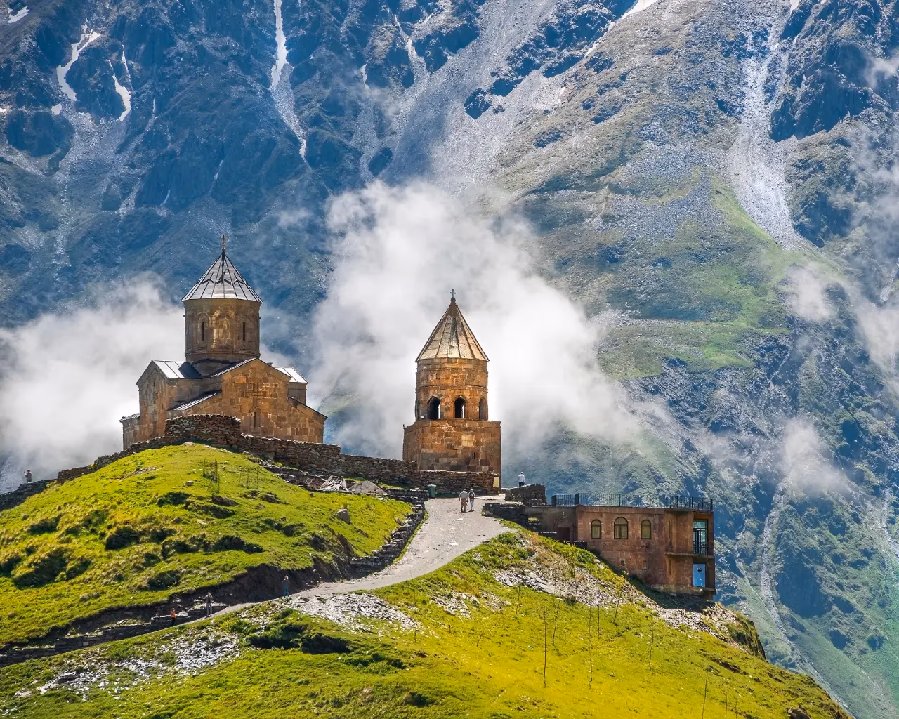 Gergeti Trinity Church - Ancient stone church atop a green hill, surrounded by misty mountains in Kazbegi, Georgia.