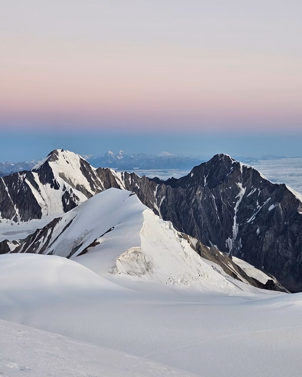Pink and blue alpenglow over jagged Mount Kazbek peaks and glaciers at sunrise.
