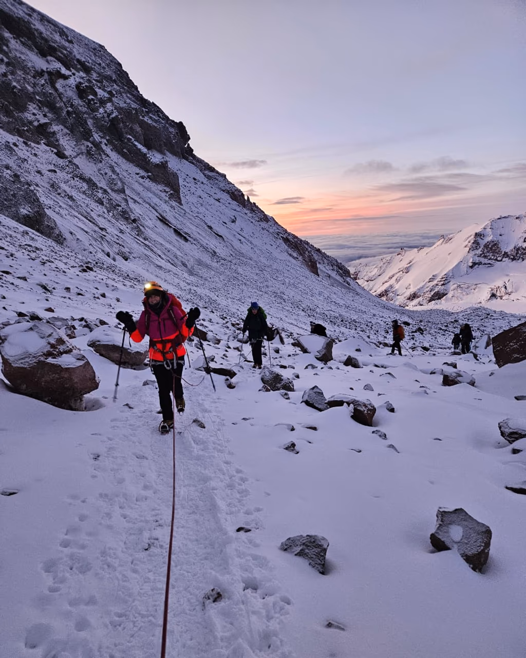 Climbers ascending snowy Mount Kazbek ridge at dawn with trekking poles and rope.