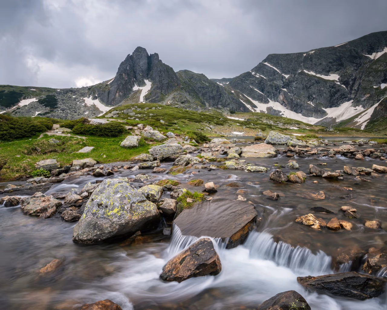 Mountain stream cascading over rocks with rugged snow-dotted peaks in Bulgaria’s Rila Mountains