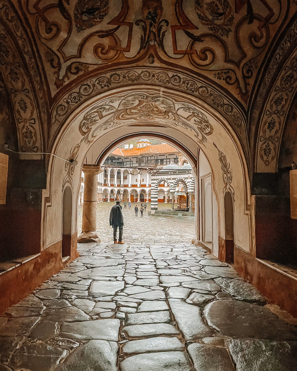A scenic view through an arched monastery entrance leading to the courtyard of Rila Monastery, Bulgaria.