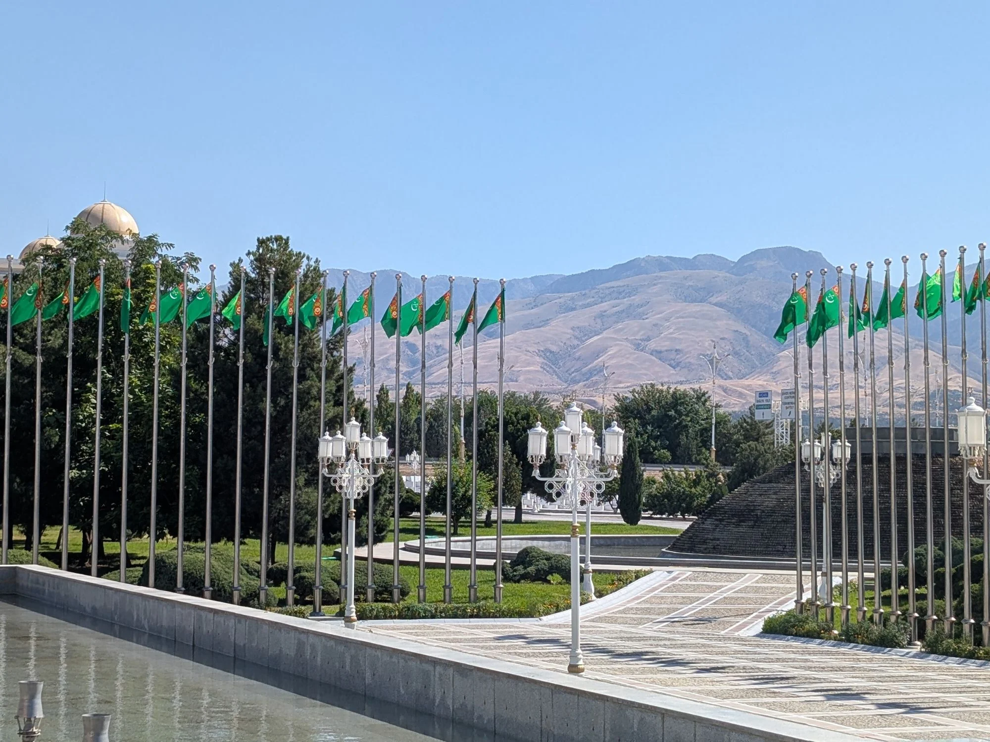 Rows of Turkmen flags lining a marble plaza with the Kopet Dag mountains behind