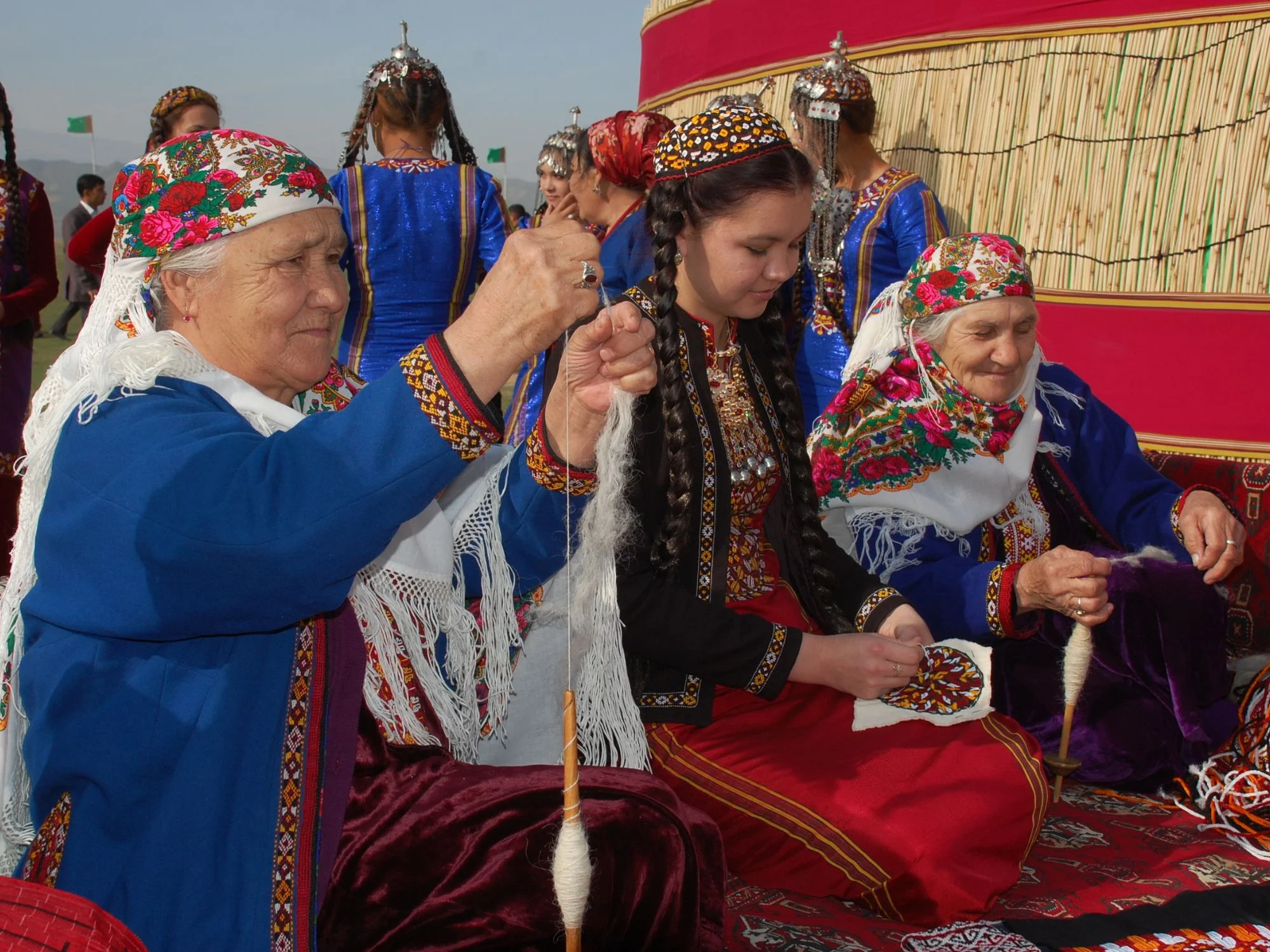 Turkmen women in traditional dress hand-spinning wool on drop spindles beside a yurt