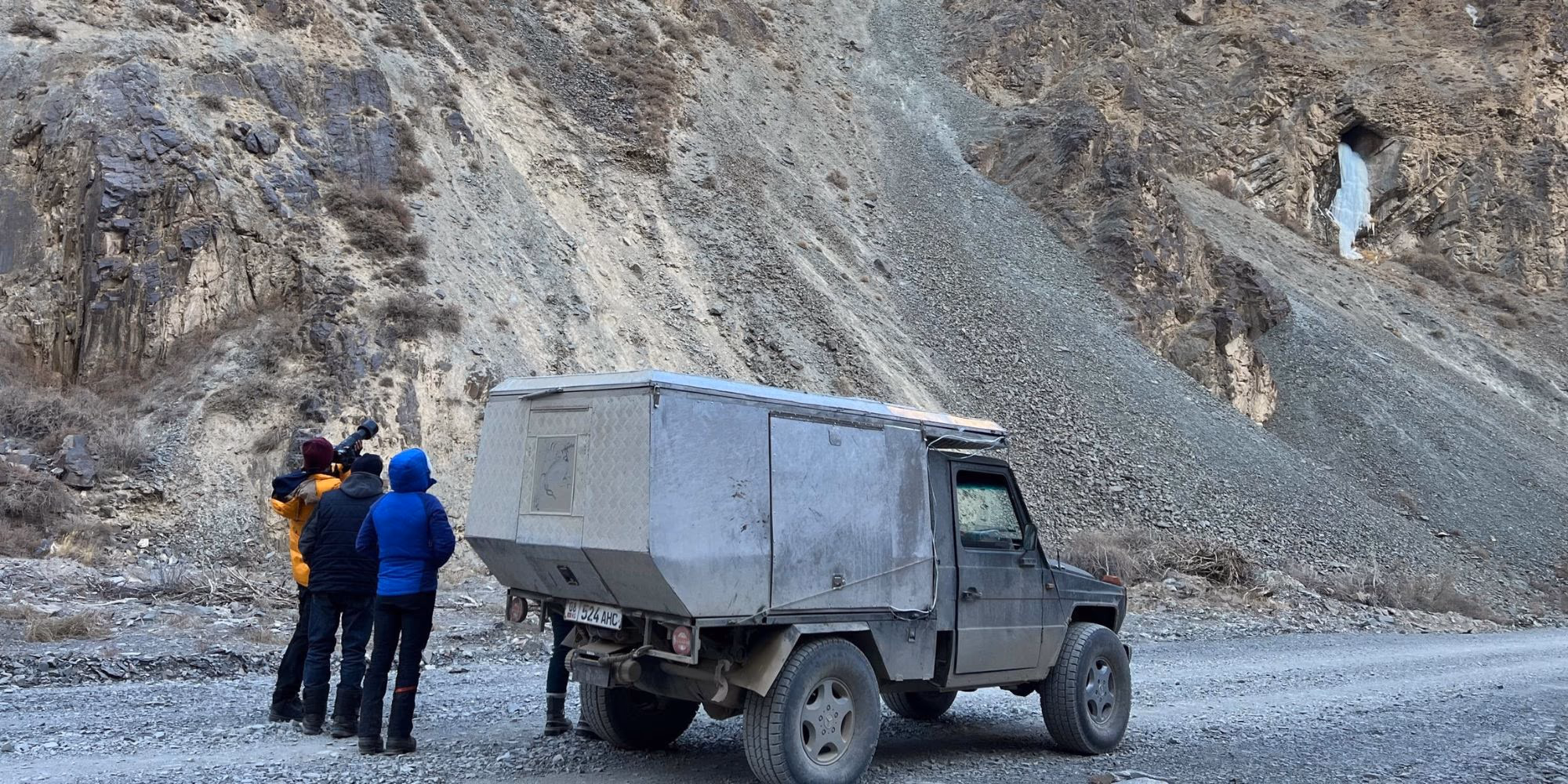 Overland 4x4 expedition vehicle and travelers exploring rugged mountain terrain on a remote adventure tour