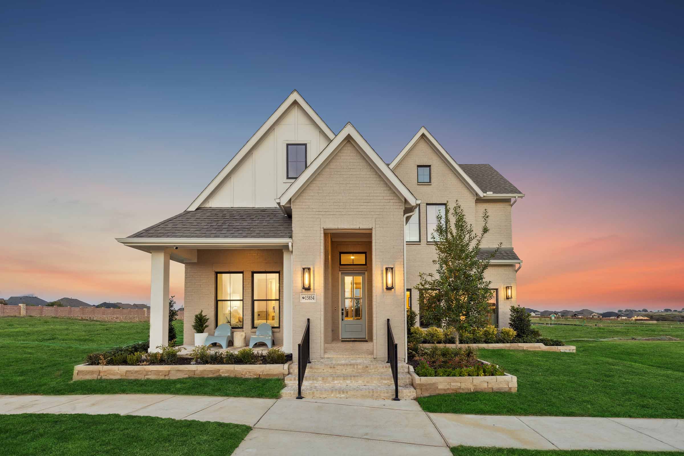 Modern two-story suburban home at sunset with landscaped front yard, large windows, and a covered porch