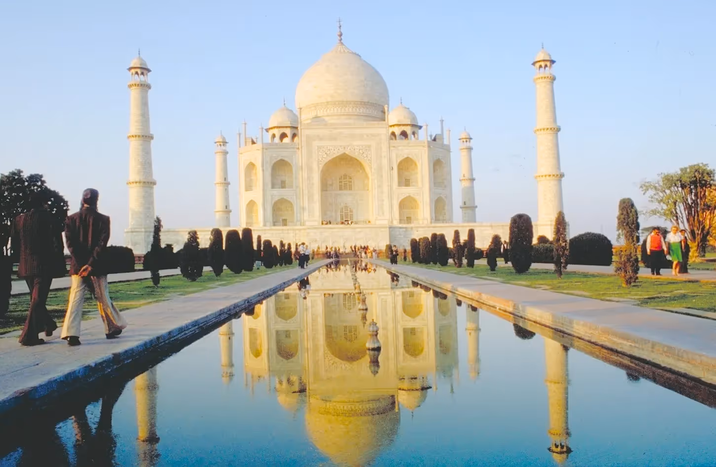 Der Taj Mahal spiegelt sich in einem langen Wasserbecken mit Besuchern auf dem Weg entlang der Gartenwege.