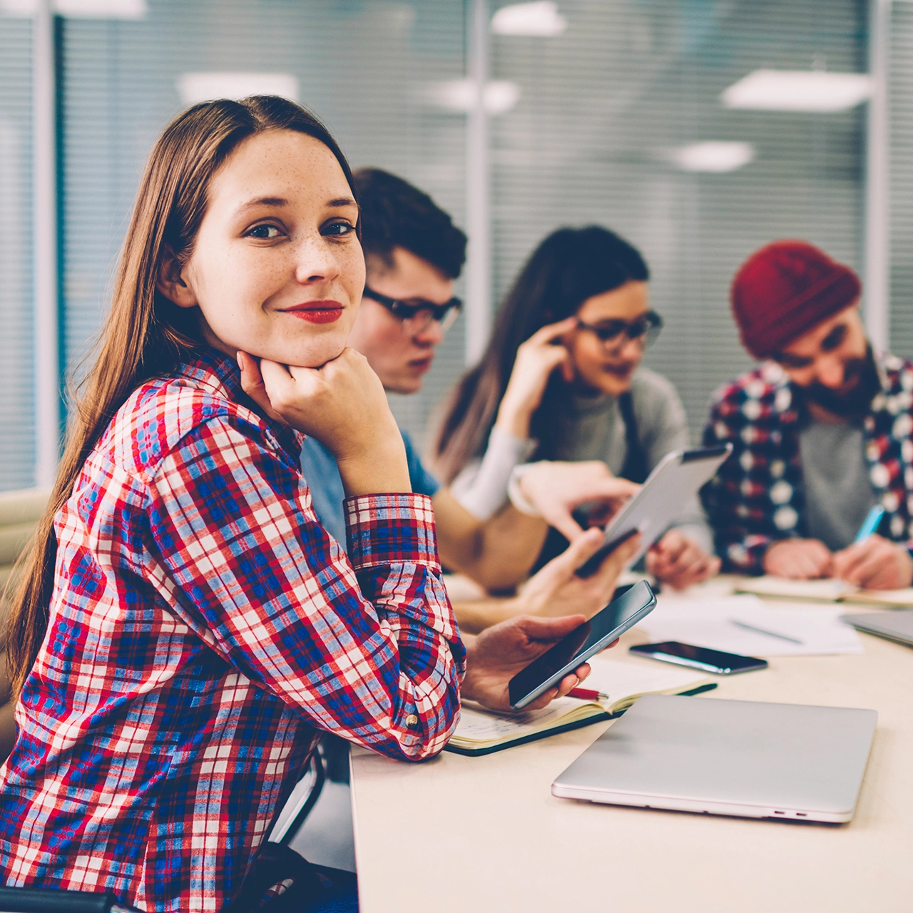 Young woman looking at camera while in a meeting with other young professionals