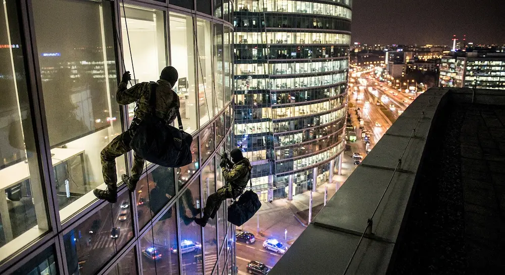 Deux espions descendent en rappel le long d'un gratte-ciel moderne de nuit au-dessus d'une ville illuminée.