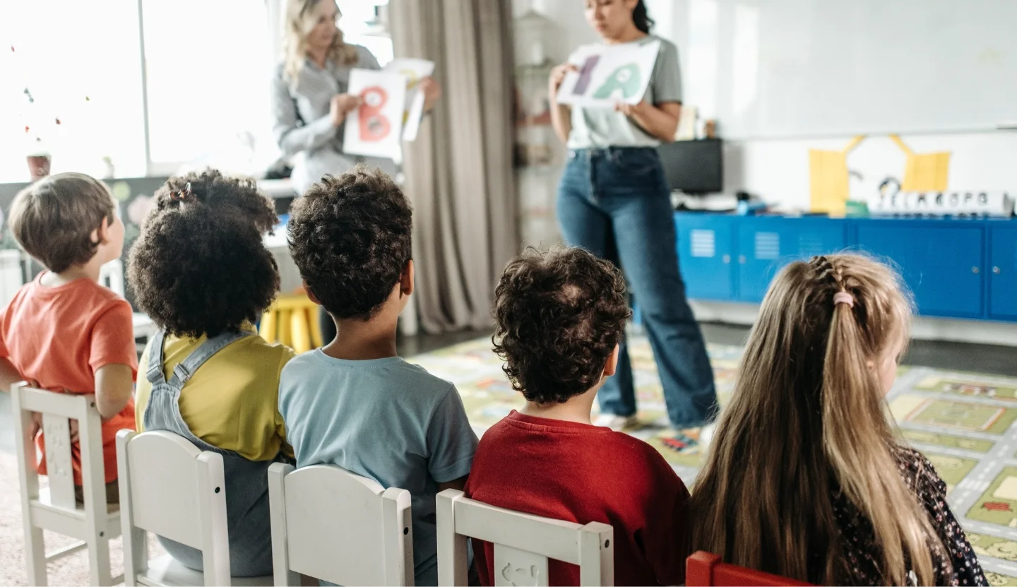 Children sitting in chairs listening to a teacher.