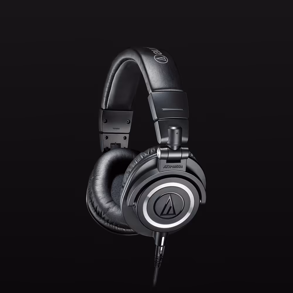 Črne naglavne slušalke čez ušesa ATH-M50x znamke Audio-Technica z oblazinjenimi ušesnimi blazinicami in naglavnim trakom na črnem ozadju.