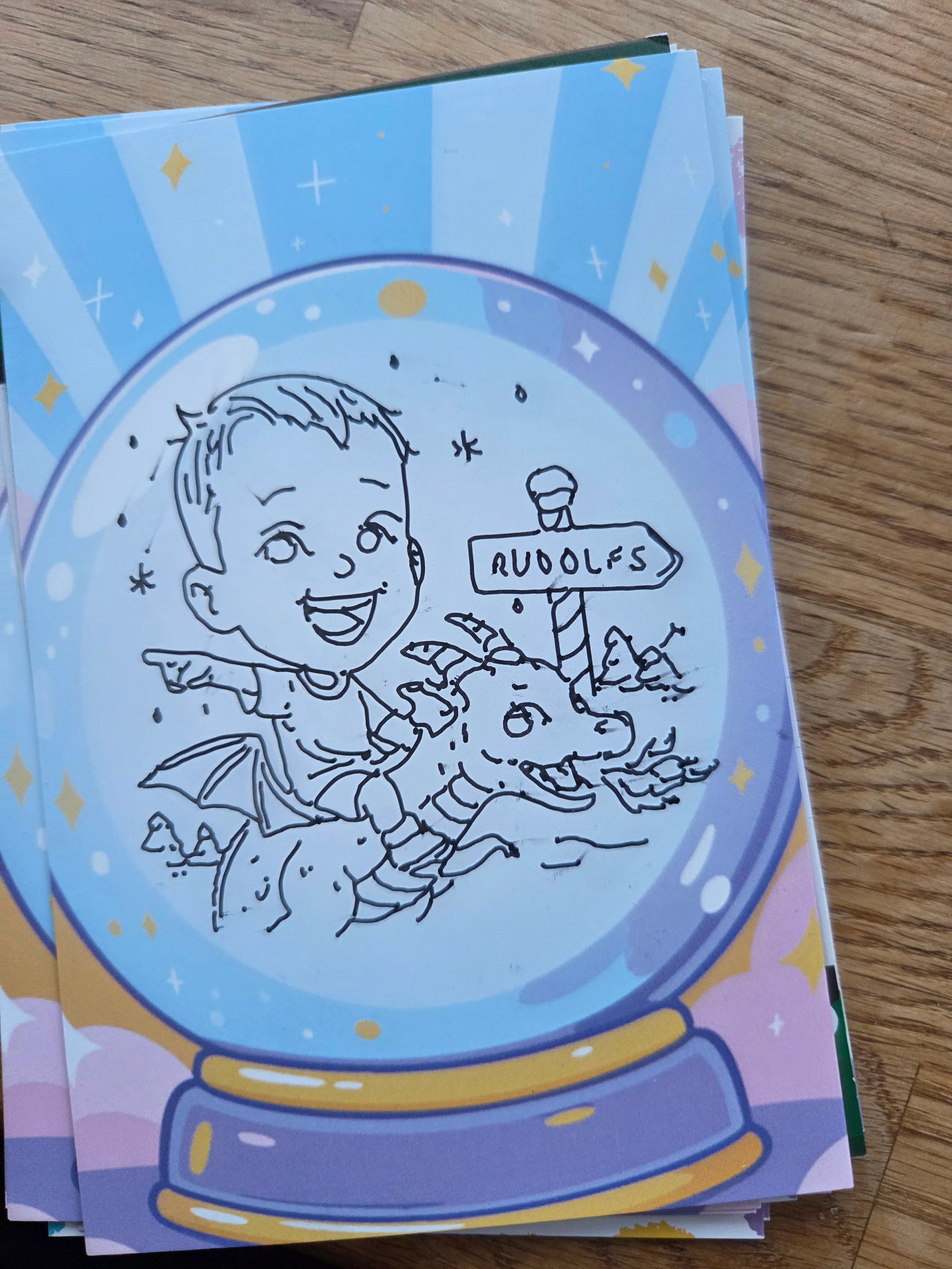 Illustration of a smiling child riding a fire-breathing dragon inside a snow globe with a sign labeled 'RUDOLFS.'
