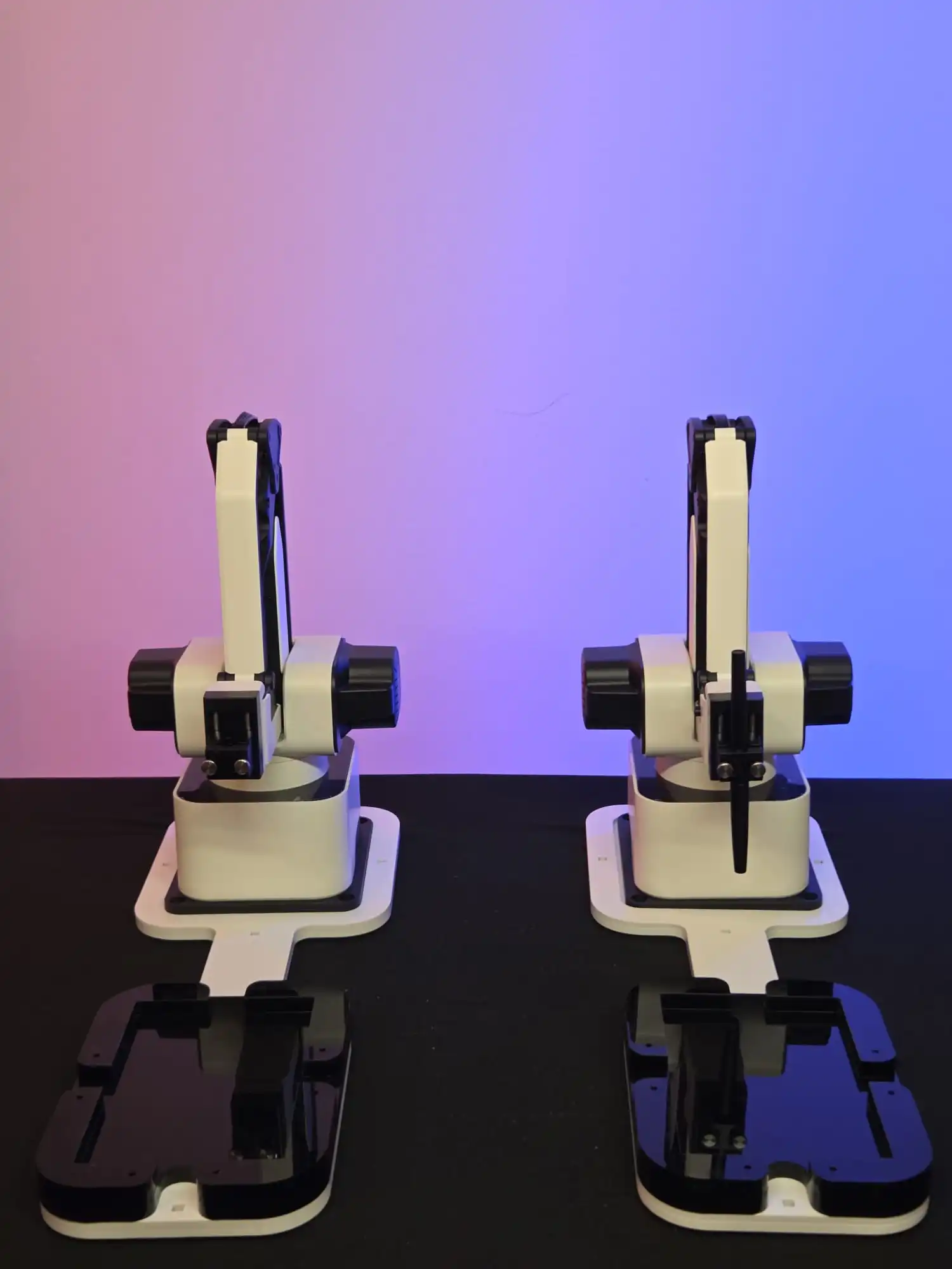 Two white and black robotic arms on a black surface with a pink and blue gradient background.