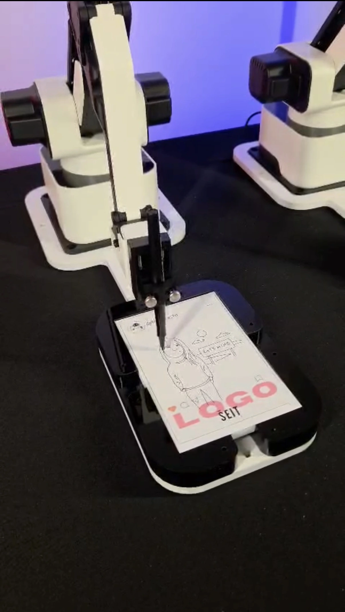 Robotic arm drawing a sketch of a person on a white paper placed on a black platform.