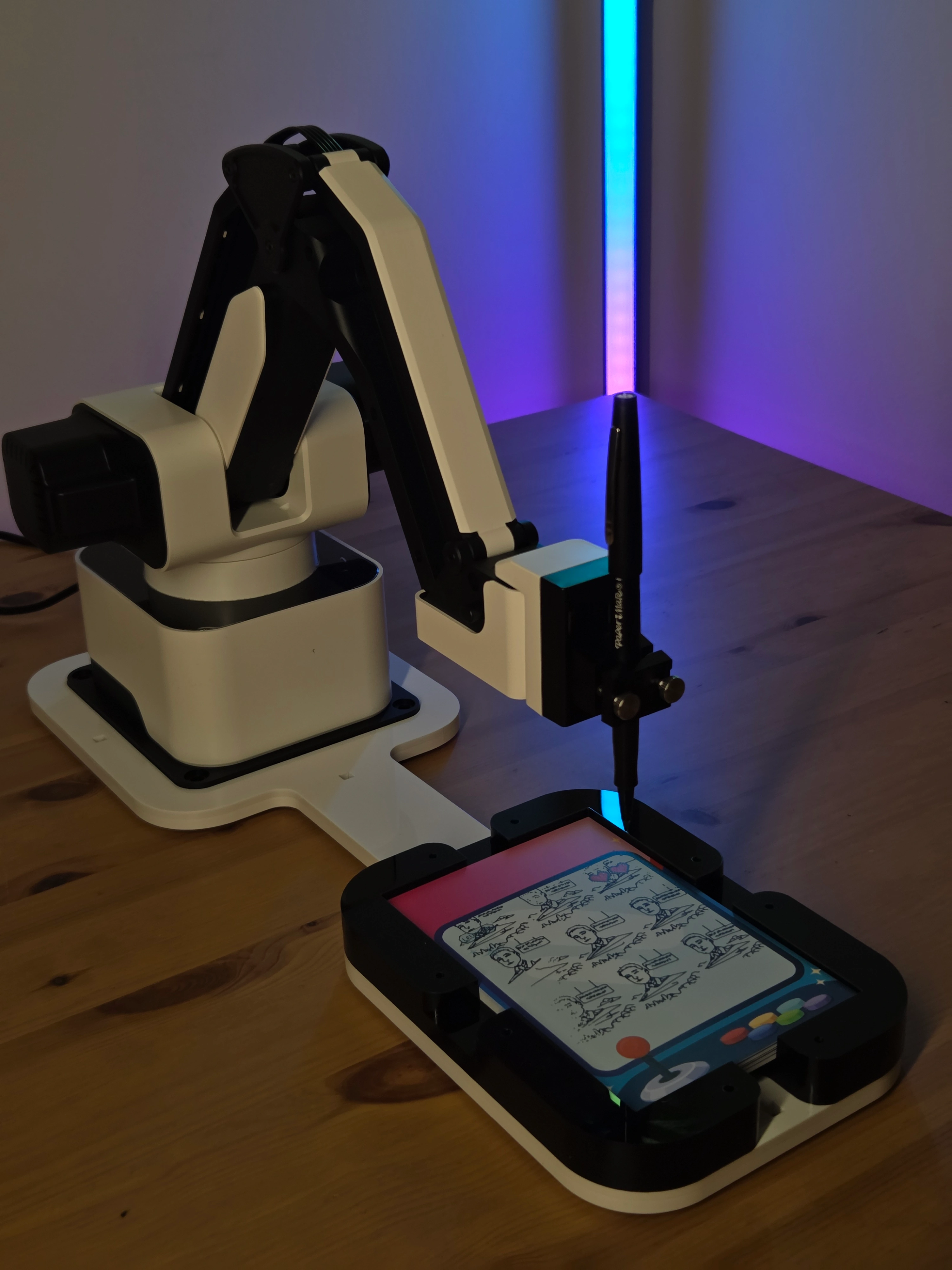 Robotic arm holding a pen drawing sketches on a retro game-themed writing pad on a wooden table with a vertical LED light strip in the background.