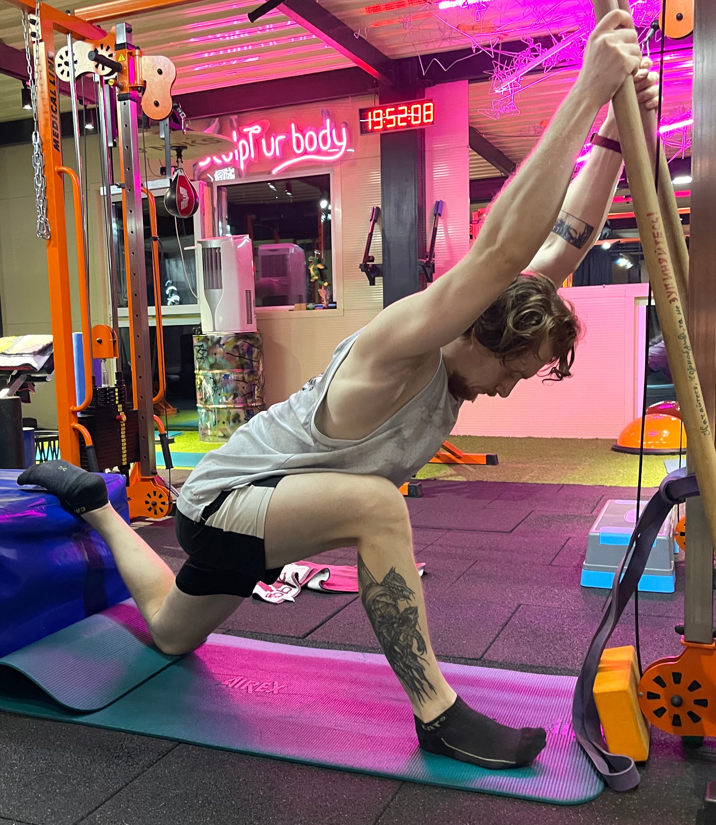 Індивідуальна сесія в Dzhevaha Gym: варіант глибокого стретчингу в положенні випаду з фіксацією плечового поясу. Позиція поєднує розтягнення згиначів стегна з роботою над мобільністю грудного відділу — зонами, що найчастіше перевантажуються при сидячій роботі. Зображення ілюструє різницю підходів у темі статичний vs динамічний стретчинг для спини. Статична фаза допомагає зменшити м’язову напругу та відновити амплітуду руху, тоді як динамічні елементи додають контроль, активують стабілізатори корпусу й формують функціональну підтримку для попереку.