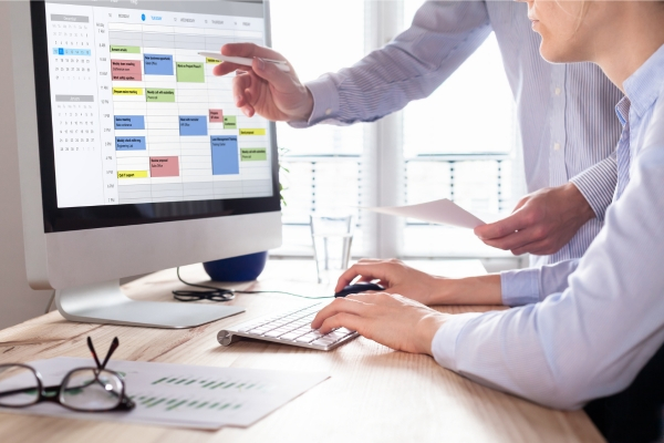 Two people reviewing a digital calendar on a computer screen to plan efficient time management