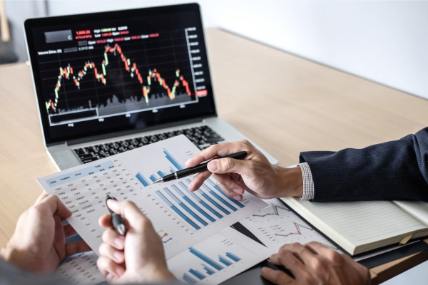 Person analyzing financial charts and data on laptop and paper reports
