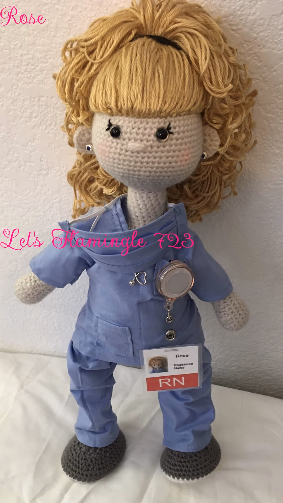 Handmade crocheted doll with blond yarn hair wearing blue nurse scrubs, gray crocheted shoes, and an RN badge.