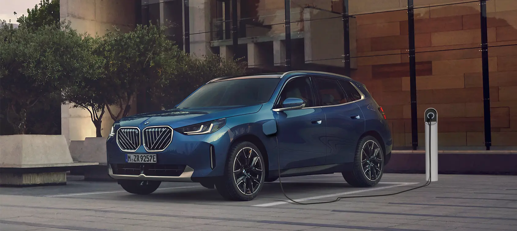 Blauer BMW SUV lädt an moderner E-Ladesäule in urbaner Umgebung – BMW Baum Automobile in Bad Neuenahr-Ahrweiler