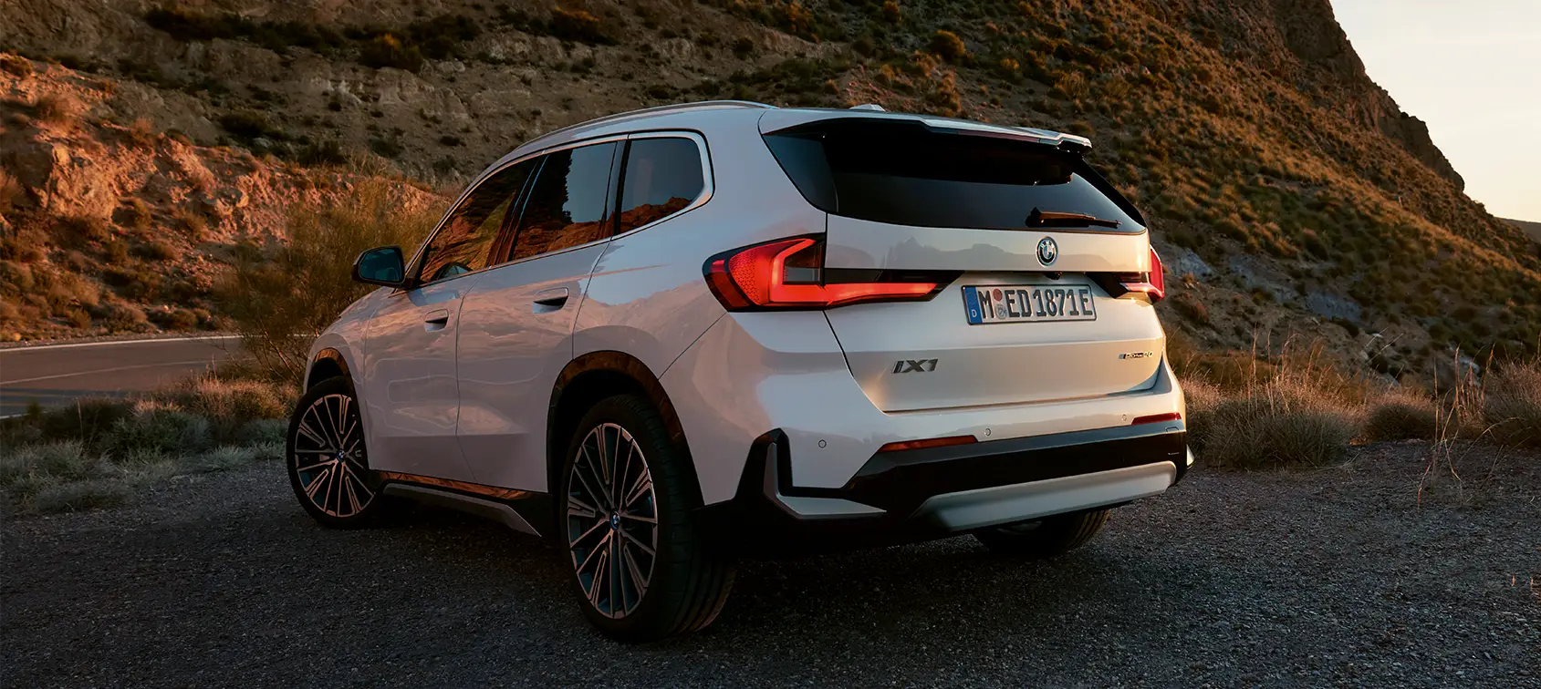 Weißer BMW iX1 geparkt in bergiger Landschaft bei Sonnenuntergang – BMW Baum Automobile in Bad Neuenahr-Ahrweiler