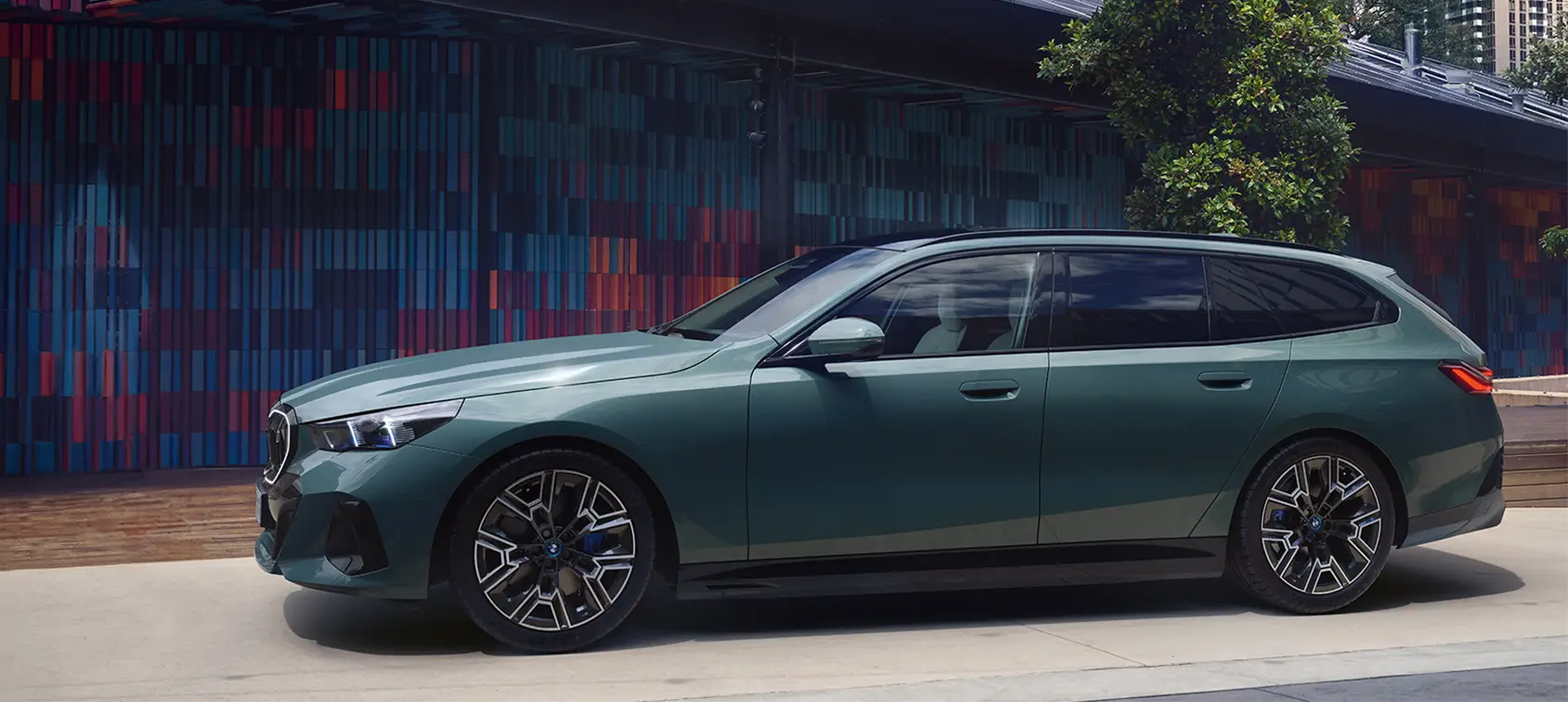 Seitenansicht eines grünen BMW i5 Touring vor moderner Architektur – BMW Baum Automobile in Bad Neuenahr-Ahrweiler