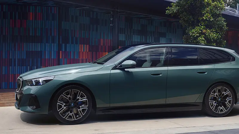 Seitenansicht eines grünen BMW i5 Touring vor moderner Architektur – BMW Baum Automobile in Bad Neuenahr-Ahrweiler
