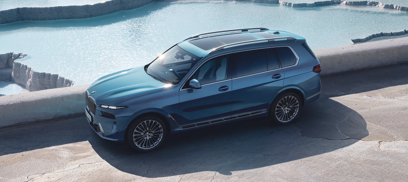BMW X7 xDrive40d in Blau, von schräg oben fotografiert, auf einer Straße neben einem hellblauen Wasserbecken – BMW Baum Automobile in Bad Neuenahr-Ahrweiler