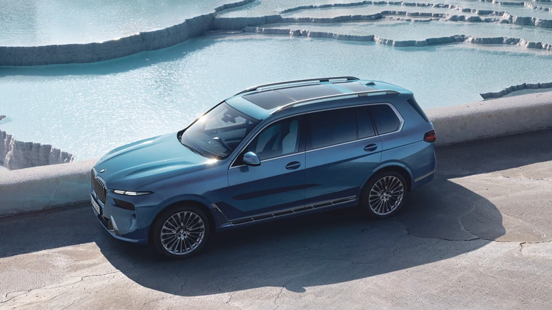 BMW X7 xDrive40d in Blau, von schräg oben fotografiert, auf einer Straße neben einem hellblauen Wasserbecken – BMW Baum Automobile in Bad Neuenahr-Ahrweiler